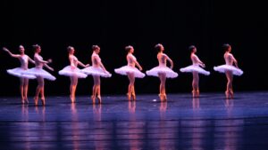 A line of dancing ballerinas in tutus on a stage.